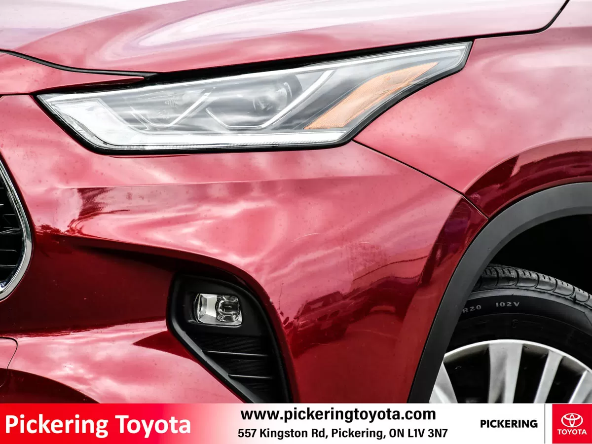 Close-up of the front headlight and fog light of a red 2022 Toyota Highlander Hybrid Limited AWD SUV parked in front of the Pickering Toyota dealershi