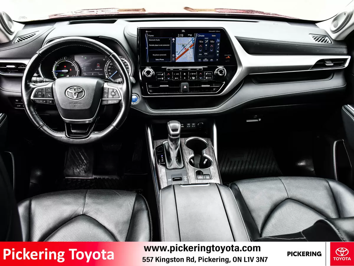 Interior view of the dashboard and steering wheel in a red 2022 Toyota Highlander Hybrid Limited AWD SUV taken at Pickering Toyota dealership.