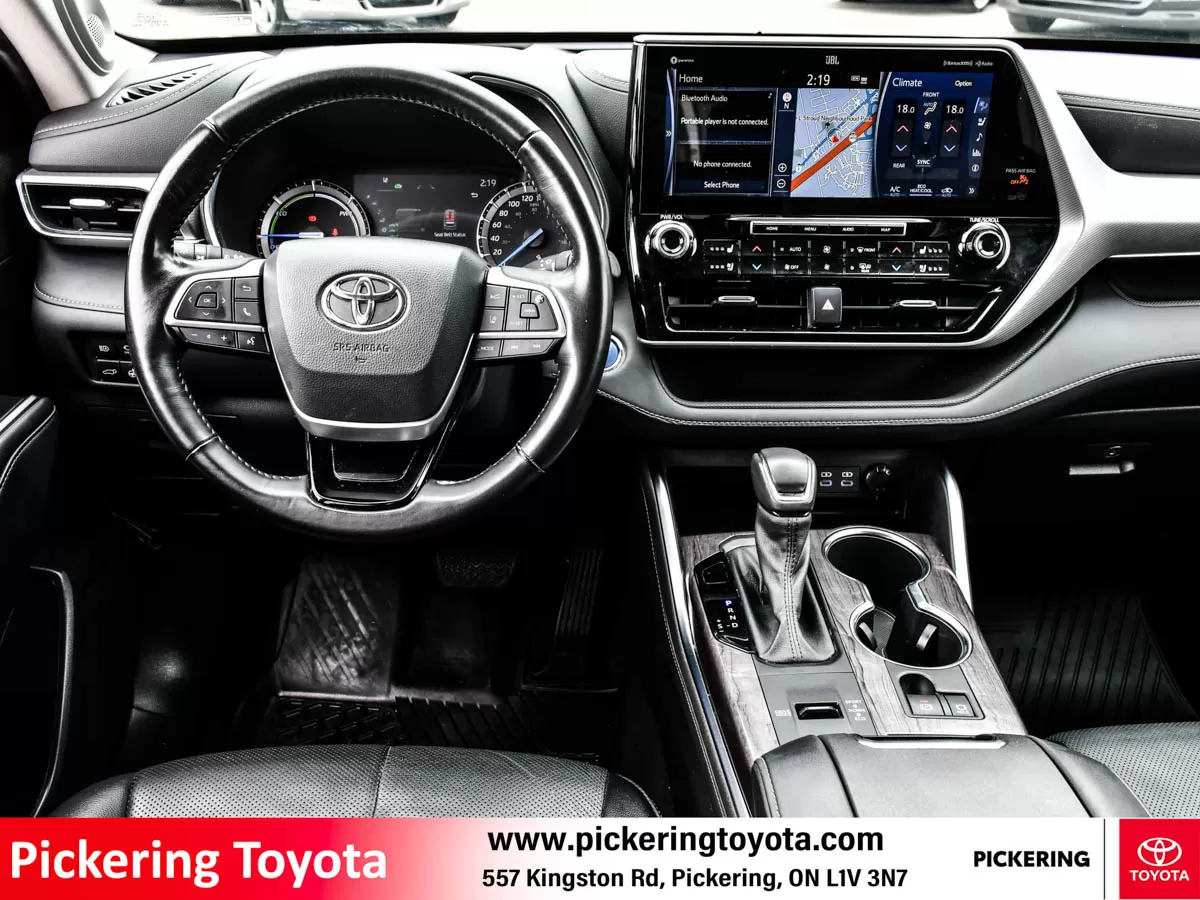 Interior view showing the steering wheel, dashboard, and central touchscreen display with the navigation system of a red 2022 Toyota Highlander Hybrid