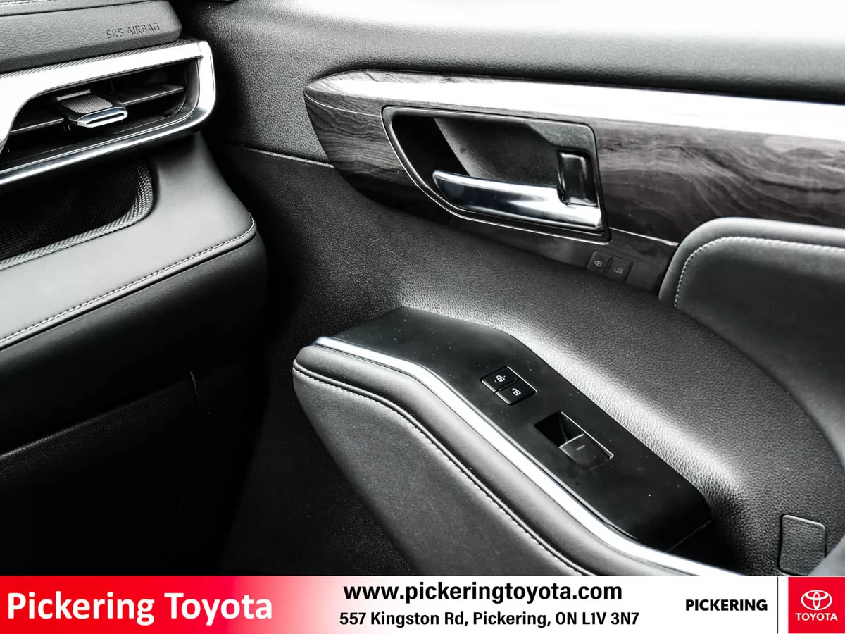 Interior view of a Toyota vehicle door panel, featuring a door handle, window controls, air vent, and SRS Airbag label, with wood and leather trim of