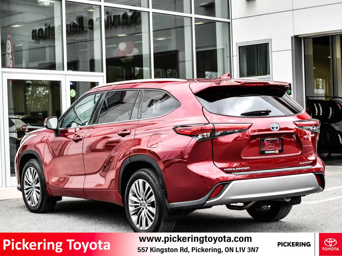 Rear side view of a red 2022 Toyota Highlander Hybrid Limited AWD SUV parked in front of the Pickering Toyota dealership