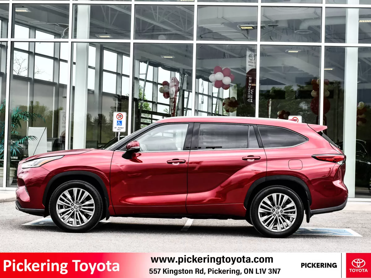 Side view of a red 2022 Toyota Highlander Hybrid Limited AWD SUV Platinum package parked in front of Pickering Toyota dealership